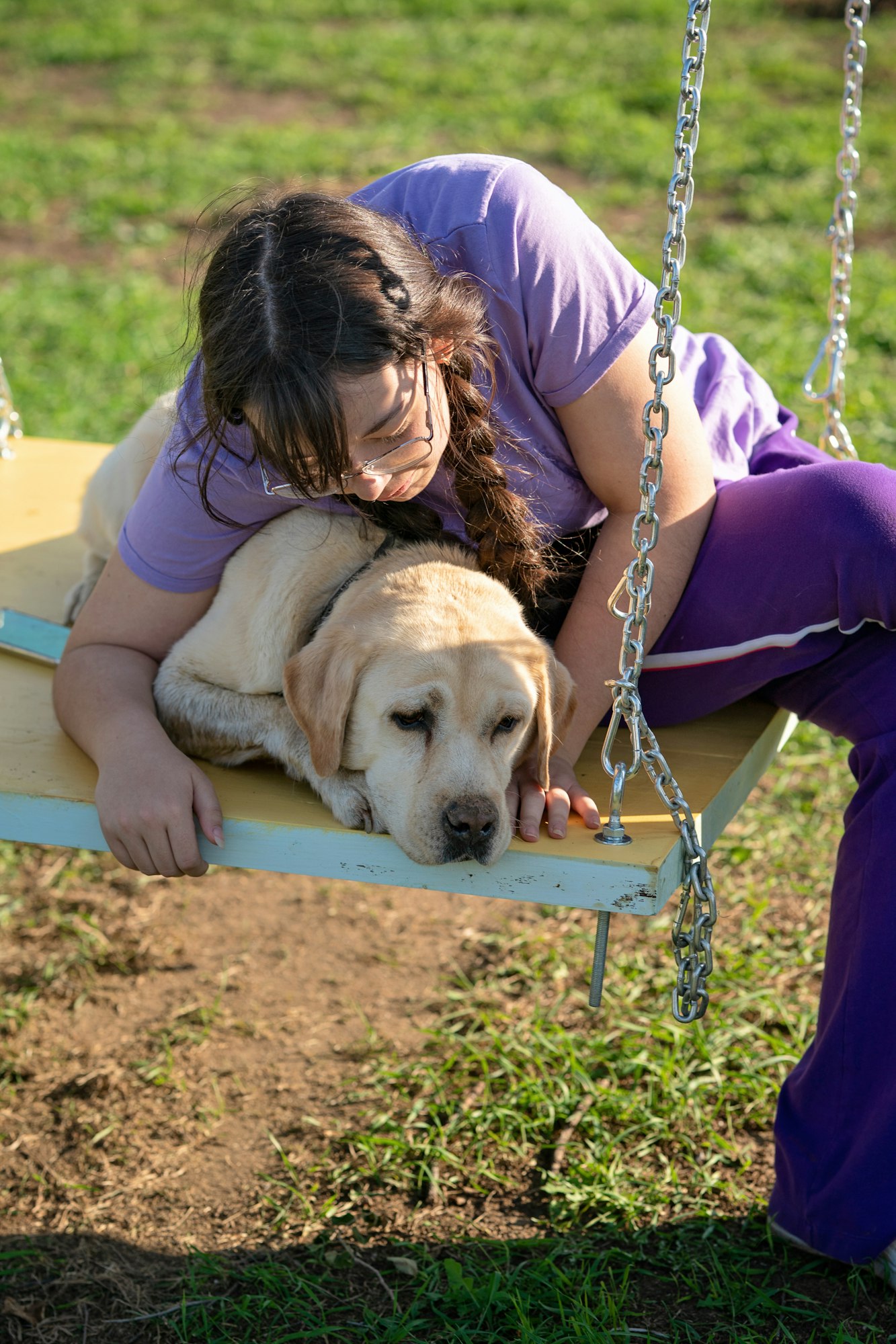 A teenage girl swings on a swing with her old Labrador dog